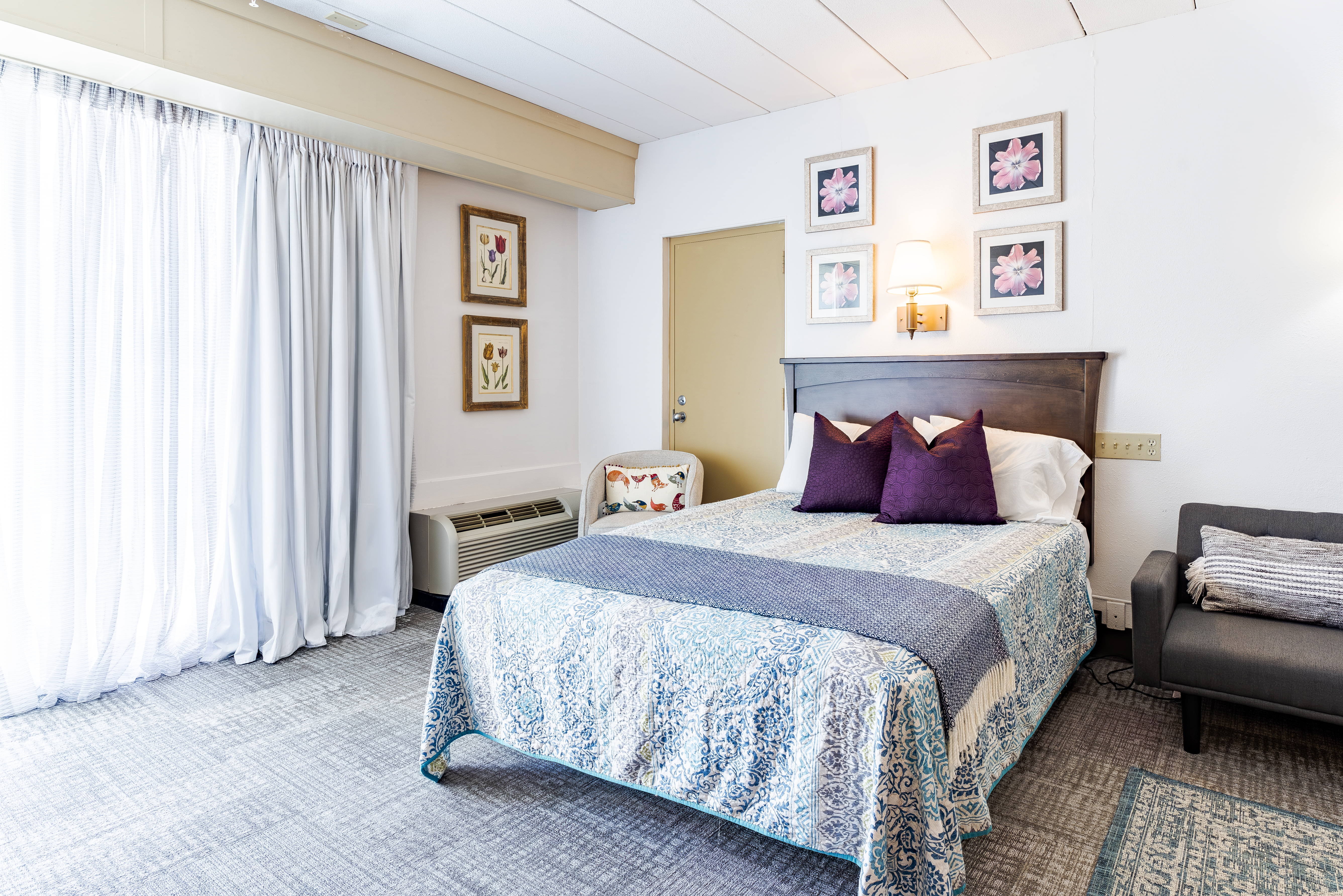 Queen bed with white curtains and patio door in furnished room at The Residences, Hadley, MA